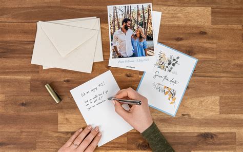 Detailná fotografia elegantnej papierovej pohľadnice položenej na drevenom stole vedľa pánskych hodiniek a pera
