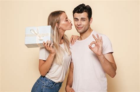 Pohľad na usmievajúceho sa muža, ktorý drží premyslený darček od partnerky, v pozadí jemne rozostrený interiér