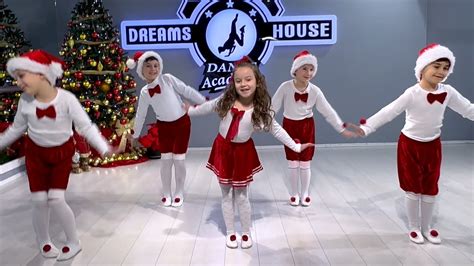 children performing christmas dances and songs on a stage decorated with a christmas tree and winter motifs