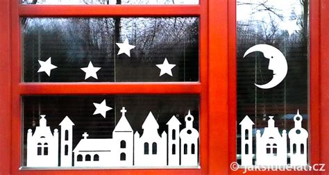 Záber na vianočne vyzdobené okno s papierovými vločkami a siluetami domčekov