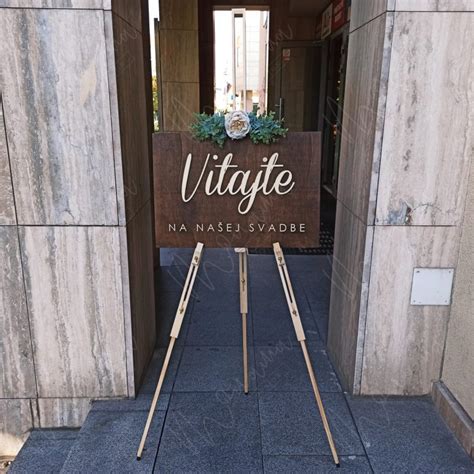 Inšpiratívna fotografia svadobnej uvítacej tabule s kvetinovou výzdobou a elegantným nápisom pri vchode do sály