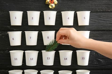 Adventný kalendár z papierových kelímkov prilepených na drevenú dosku.