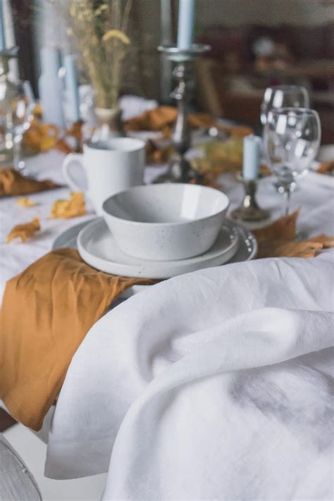 Detail minimalistického prestierania: biely obrus, jeden žltý kvet vo váze, zelený eukalyptový list a ľanový obrúsok