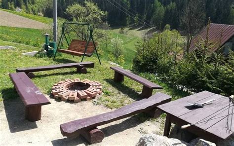 Fotografia exteriéru s ohniskom a drevenými pníkmi na sedenie, v pozadí hory.