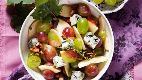 Detailný záber na misu s prémiovými syrmi, hroznom a orechmi, dekorovanú červenými kvetmi a elegantnými menovkami