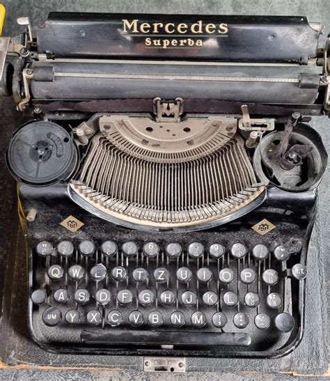 Tematická fotografia: Starý písací stroj s rozpracovaným textom prejavu a kytica tmavých kvetov, symbolizujúca prípravu na poslednú rozlúčku.