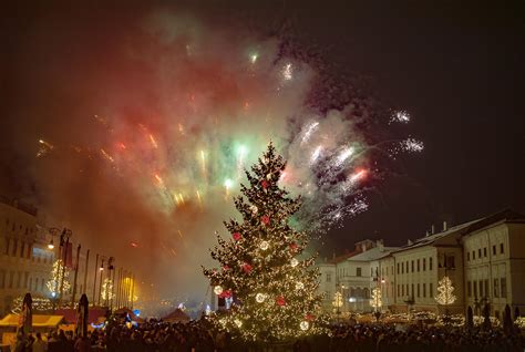 Tematická fotografia: Dav ľudí na námestí oslavujúci Silvester s ohňostrojom v pozadí