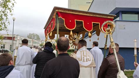 Katolícka eucharistická procesia s monštranciou a kňazom v čele, s veriacimi a deťmi rozsýpajúcimi kvety