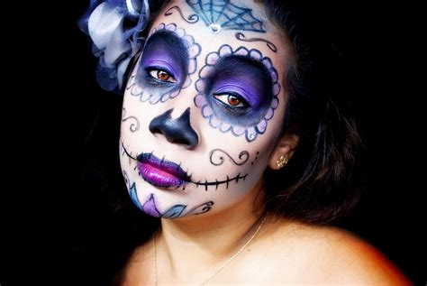Portrét ženy s detailným líčením Sugar Skull (Cukrová lebka) na tvári, s farebnými ornamentami a kvetinovou čelenkou.