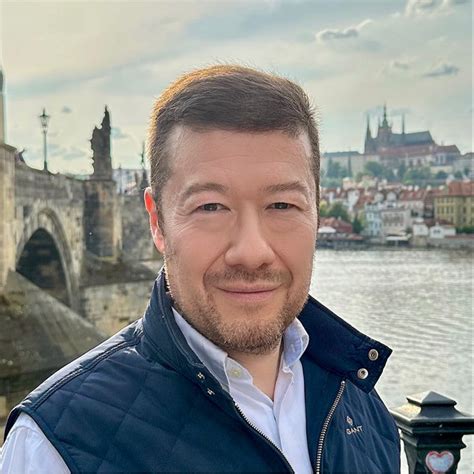 muž prednášajúci prejav s mikrofónom, v pozadí usmievaví hostia
