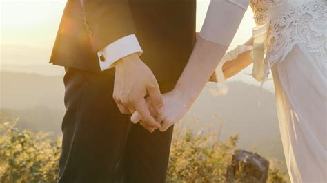 Zblízka záber na ruky snúbencov s prsteňmi počas zasnúbenia, kňaz žehná.