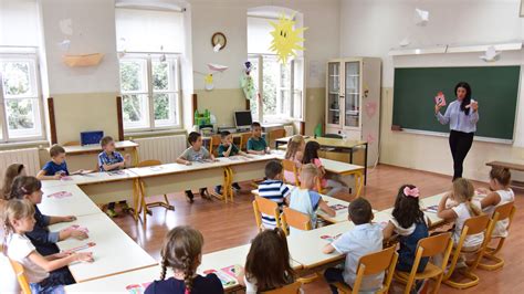 Fotografia starých školských lavíc v prázdnej triede, s lúčmi slnka prenikajúcimi cez okno, symbolizujúca plynutie času.