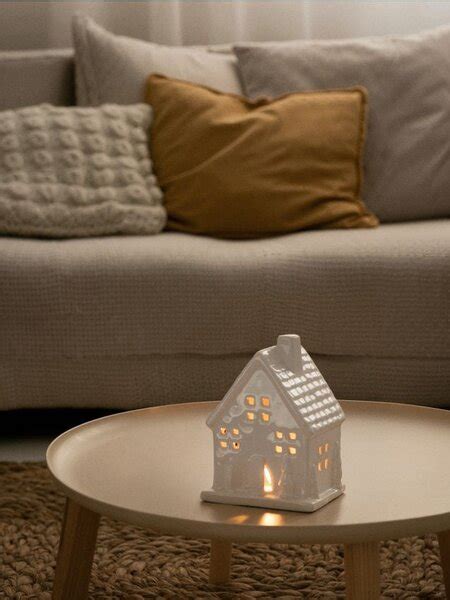 Detail kovového svietnika v tvare domčeka s hrdzavým korténovým efektom, zdôrazňujúci prepracované výrezy