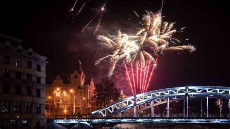 Ilustrácia zobrazujúca farebné ohňostroje nad siluetou mesta, symbolizujúce oslavu Nového roka.