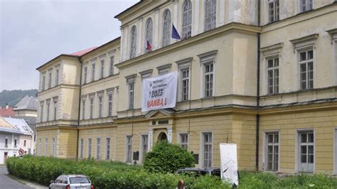 Skupina absolventov spoločne drží transparent a smeje sa, v pozadí je školská budova
