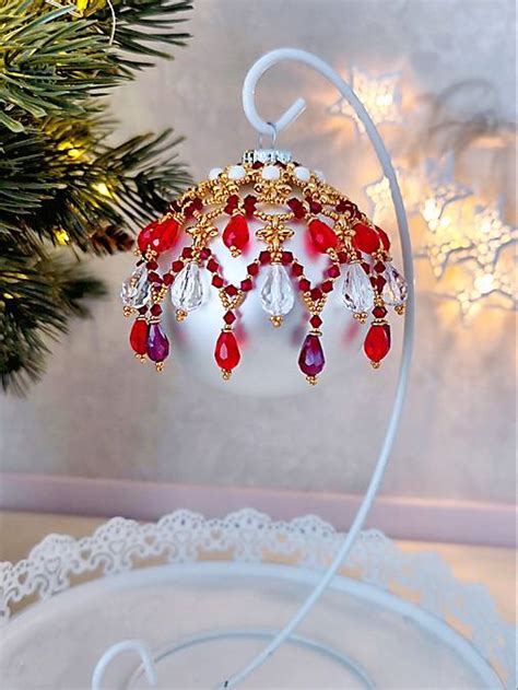 Detailný záber na ručne zdobenú sklenenú vianočnú guľu so zlatými prvkami na vianočnom stromčeku