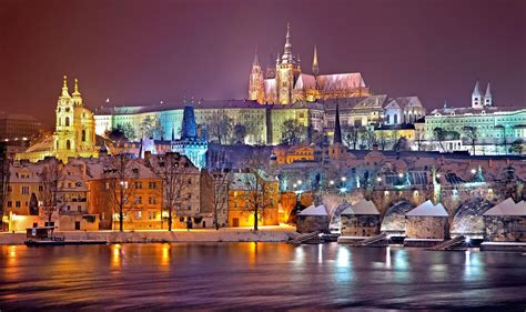 Ľudia korčuľujúci na vonkajšom klzisku s výhľadom na Pražský hrad v pozadí