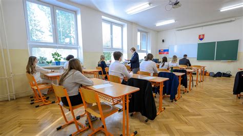Slávnostne vyzdobená školská aula s kvetinovou výzdobou a skupinou maturantov počas rozlúčky