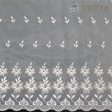 Detailný záber na jemnú bielu záclonu s vyšívanými snehovými vločkami, cez ktorú presvitá zimné slnečné svetlo v útulnej obývačke