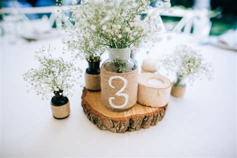 Detail výzdoby svadobného stola s ľanovým obrusom, lúčnymi kvetmi v zaváraninových pohároch a drevenými podnosmi