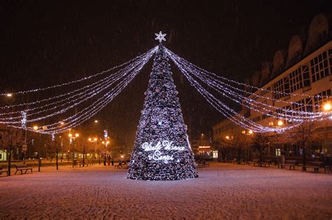 Ilustrácia zobrazujúca zasneženú dedinu s vianočne vyzdobenými domami a horiacimi lampášmi.