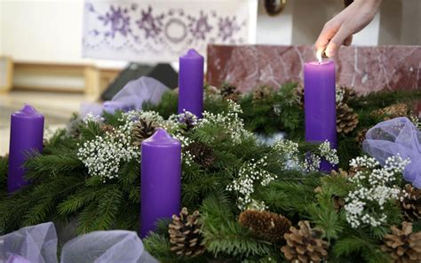 fotografia adventného venca so štyrmi zapálenými sviečkami, tromi fialovými a jednou ružovou
